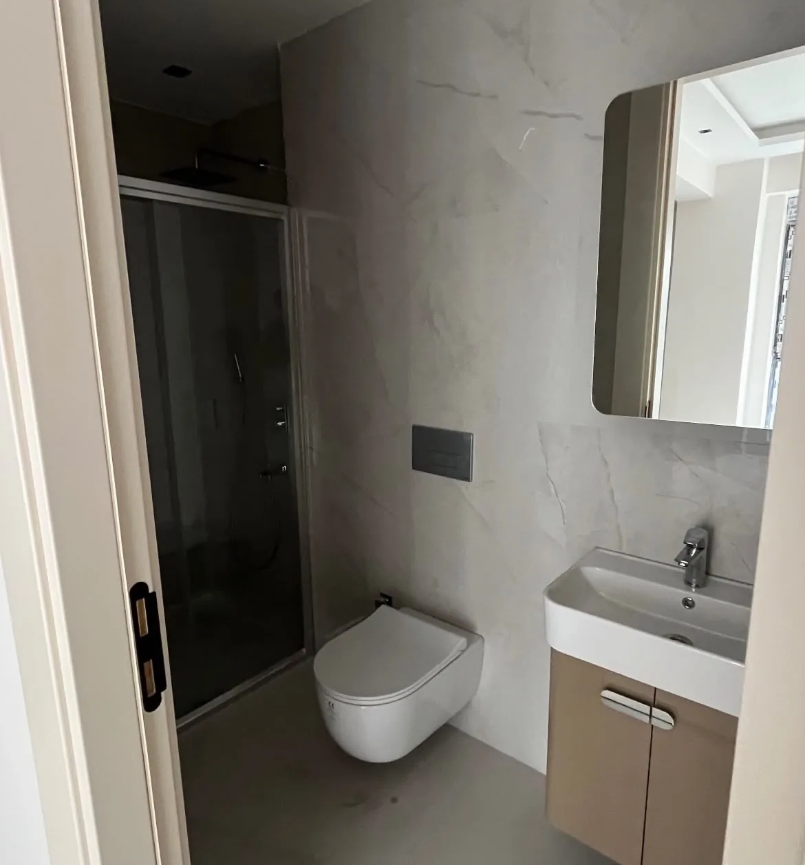 Tepebaşı Batıkent Mahallesi'nde yenilenen banyo: mermer görünümlü karolar, asma klozet, füme camlı duş kapısı ve bej lavabo dolabı, 2026