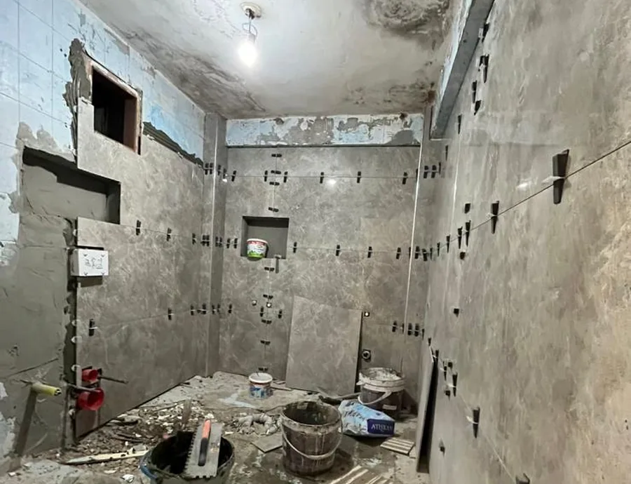 Odunpazarı Gökmeydan Mahallesi'ndeki banyo iş sürerken: eski açık mavi karolar yer yer sökülmüş, duvarlara gri karolar döşeniyor, zeminde kova ve moloz, 2026