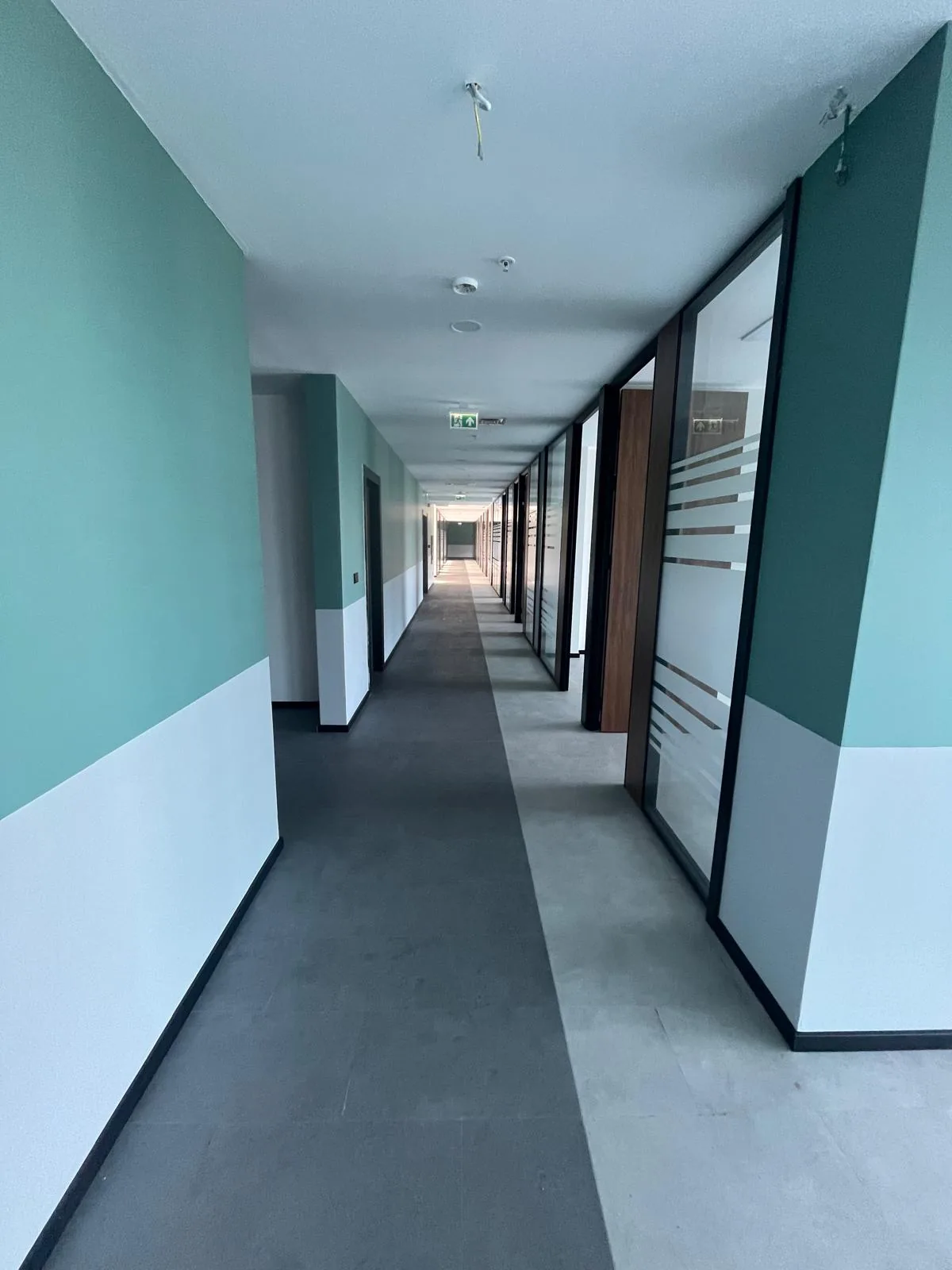 Odunpazarı Eskişehir OSB'deki Alp Havacılık ofis koridoru geniş açıdan: cam bölmeler, yeşil-beyaz duvarlar ve tavanda bağlanmamış kablo uçları, 2026