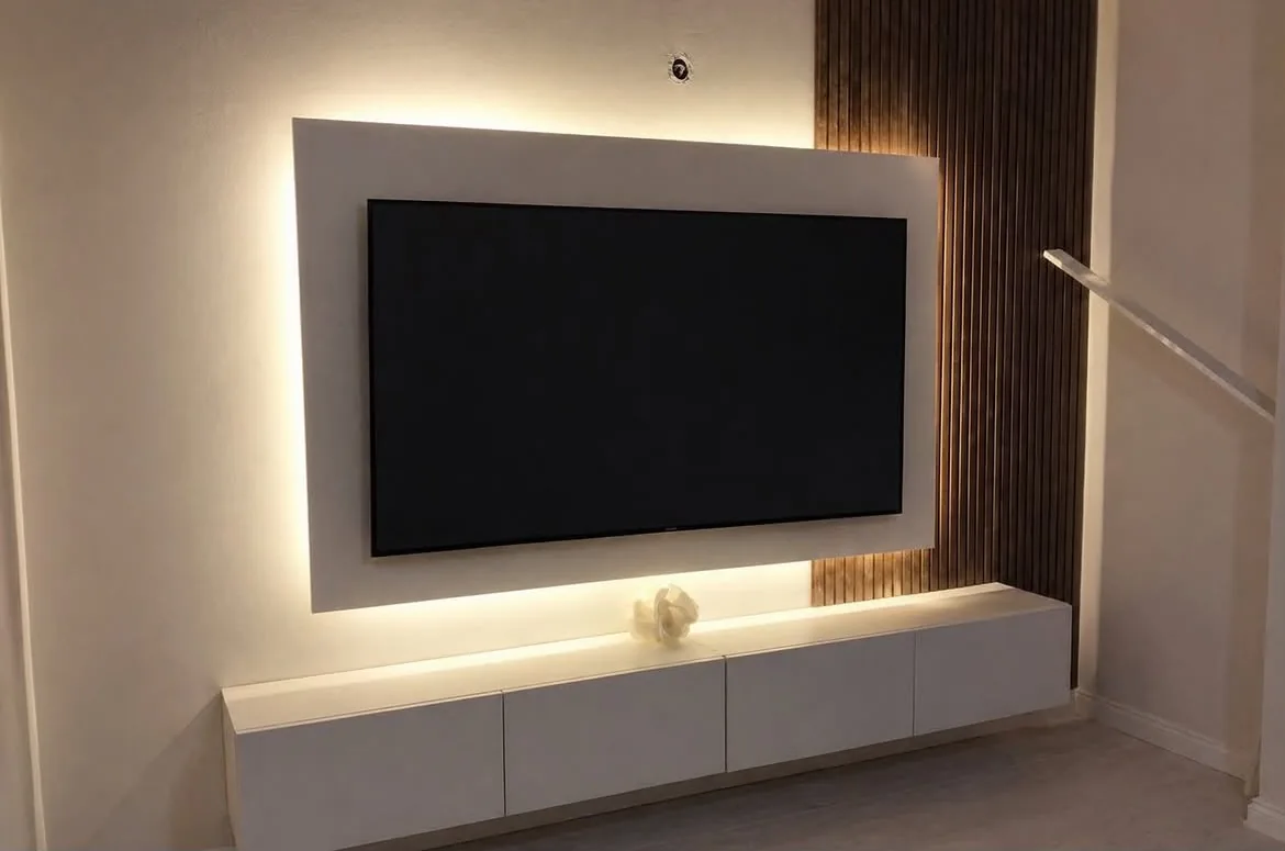 Tepebaşı Batıkent Mahallesi'nde yapılan TV ünitesi: arkadan aydınlatmalı beyaz panel, dikey ahşap lamel ve duvara asılı beyaz alt modül, 2026